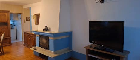 A living room with a fireplace, wooden cabinets, a television on a stand, and a kitchen in the background.