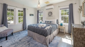 A bedroom with a large bed, two bedside tables, a chandelier, and a view of trees through the windows. - Agate Ranch | 2 BD + Views + EV + Walk to River (Three Rivers)