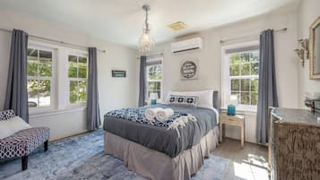 Ein Schlafzimmer mit einem großen Bett, zwei Nachttischen, einer Chandelüster und Blick auf Bäume durch die Fenster.