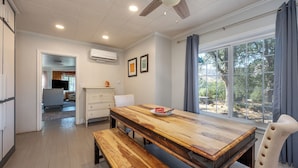 A dining area with a wooden table and bench, a ceiling fan, and a view of the outdoors through large windows. - Agate Ranch | 2 BD + Views + EV + Walk to River (Three Rivers)