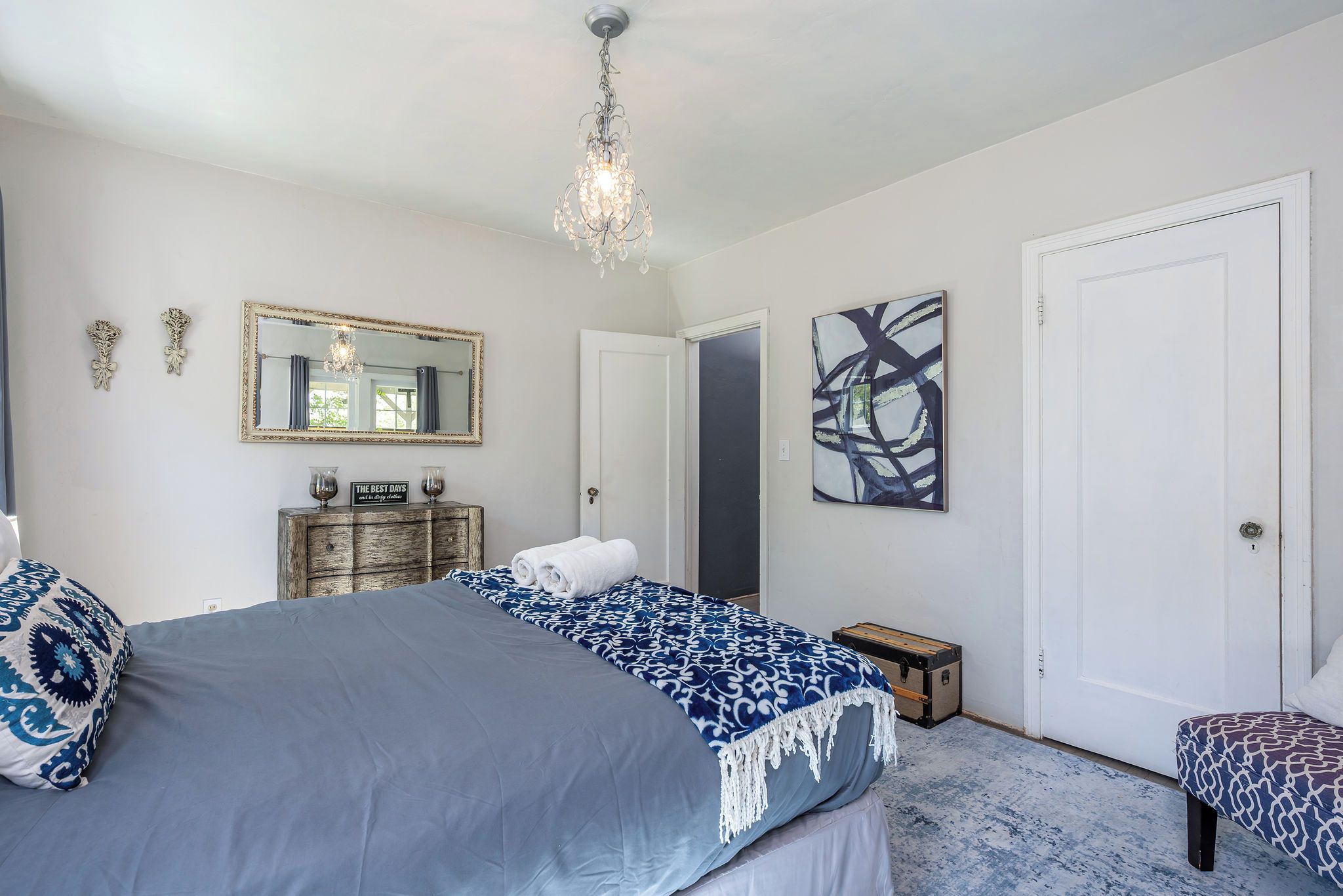 A bedroom with a large bed, a dresser, a mirror, and a chandelier.