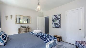 A bedroom with a large bed, a dresser, a mirror, and a chandelier.