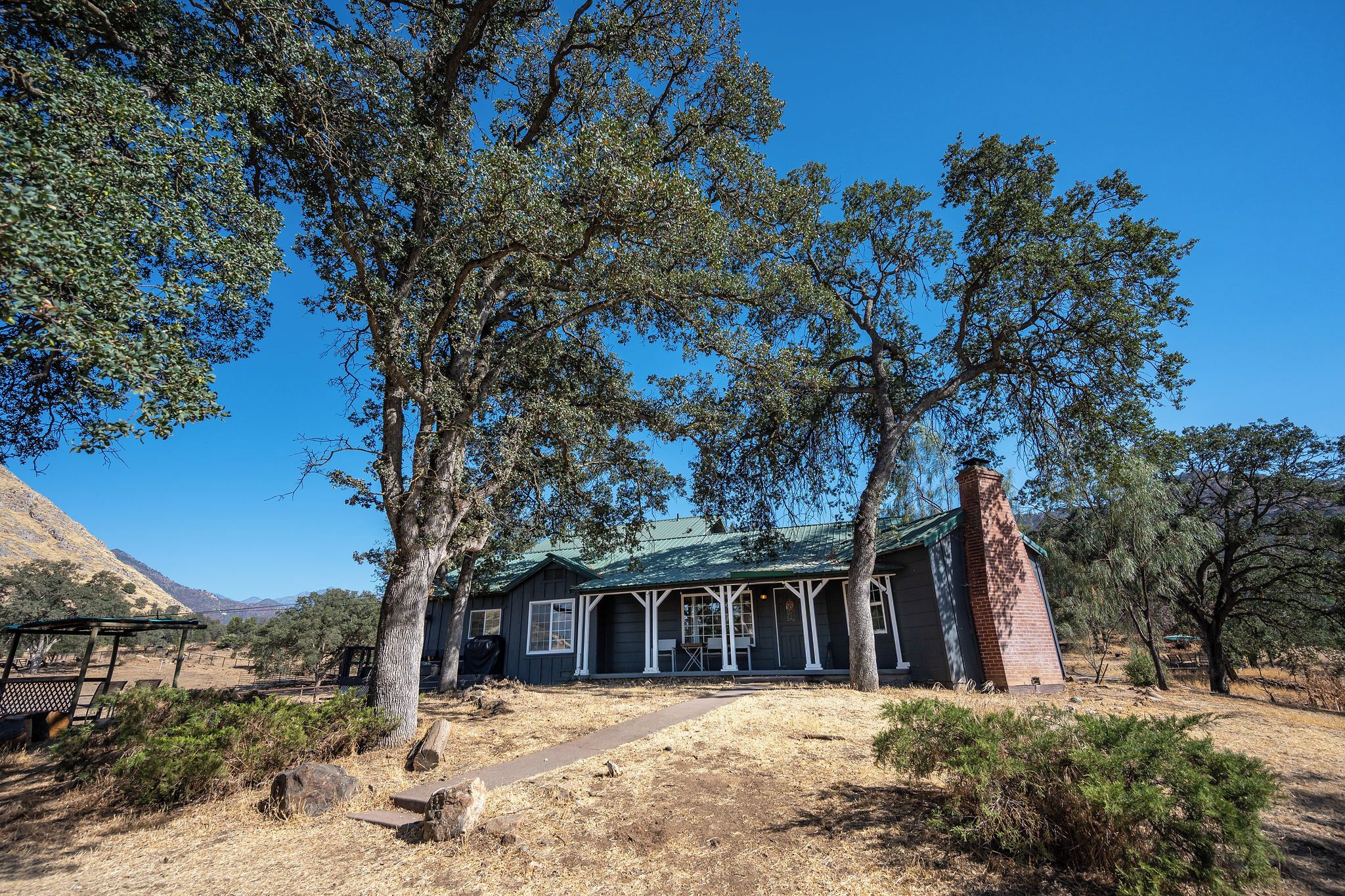 Un edificio rústico con una chimenea de ladrillo, rodeado de árboles y un paisaje seco.