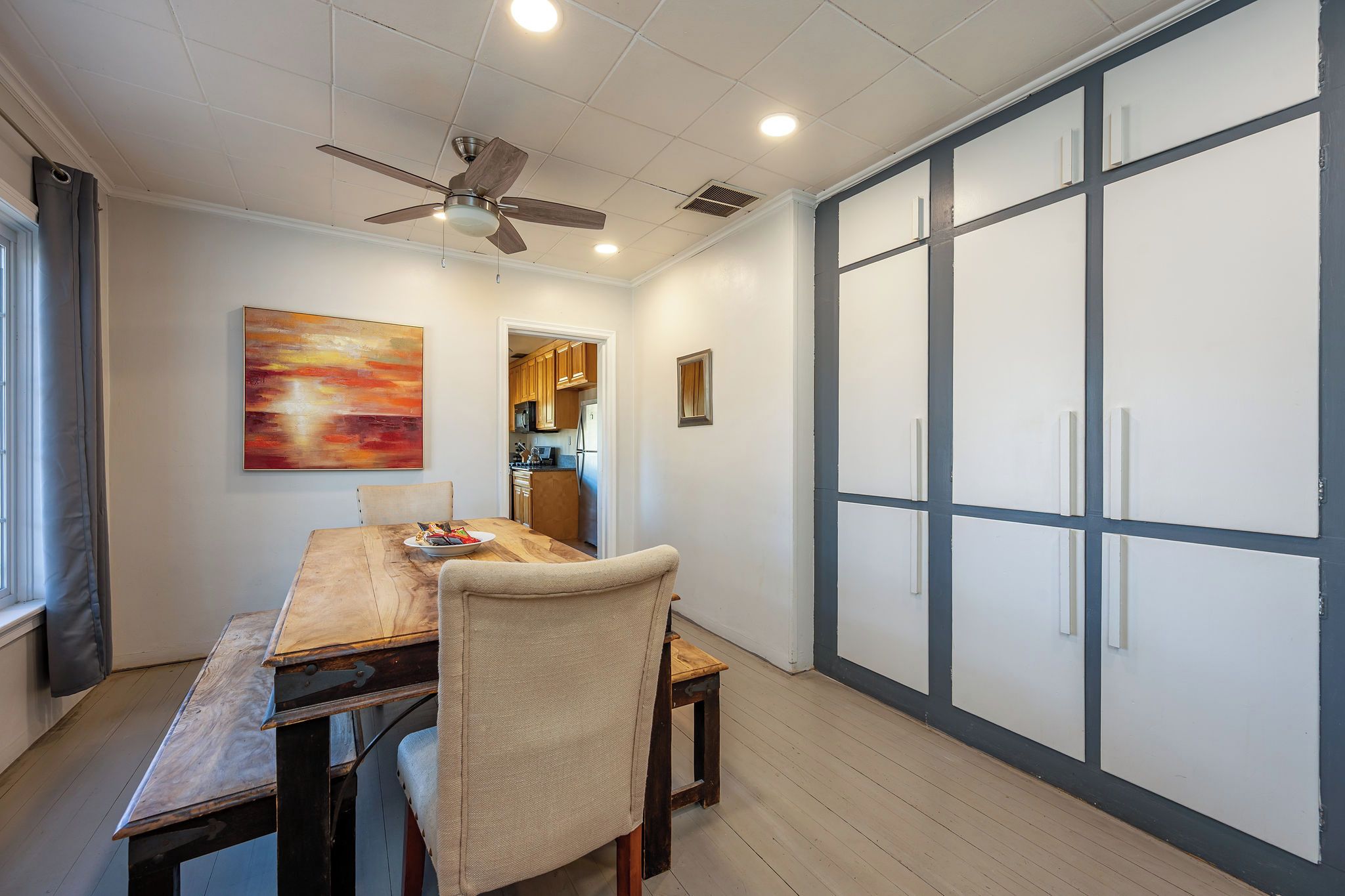 A dining area with a wooden table, chairs, a ceiling fan, and a view into the kitchen.