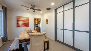 A dining area with a wooden table, chairs, a ceiling fan, and a view into the kitchen.