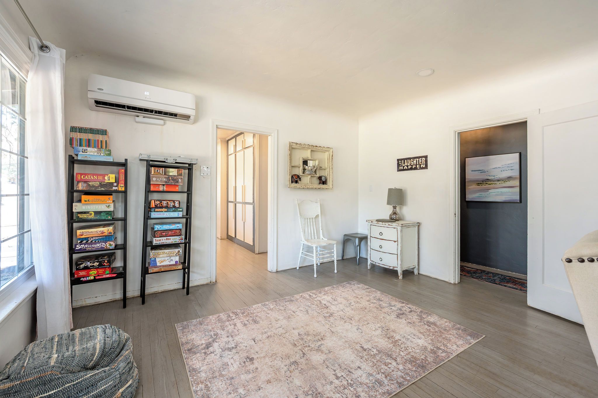 A room with a bookshelf, a desk, a chair, a rug, and an air conditioning unit.