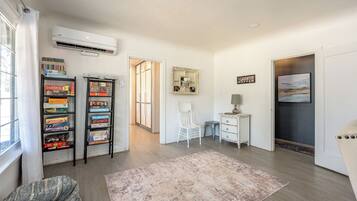 A room with a bookshelf, a desk, a chair, a rug, and an air conditioning unit.