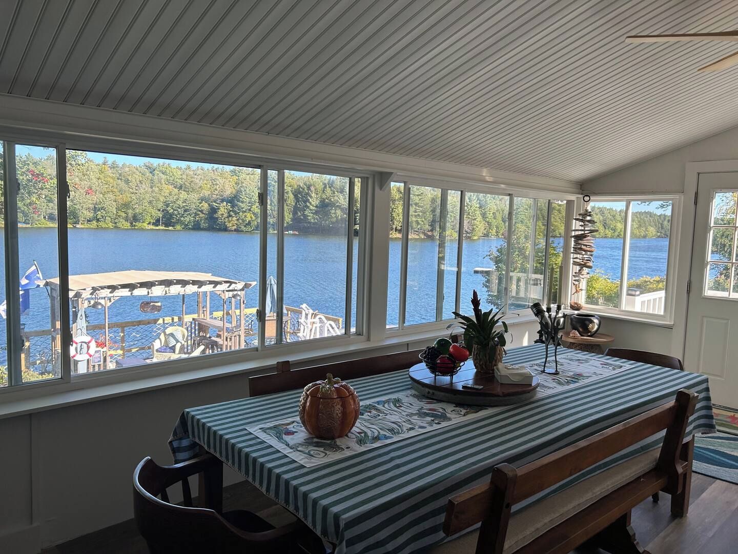 A dining area with a view of a lake, a table with a striped tablecloth, and a large decorative pumpkin centerpiece.