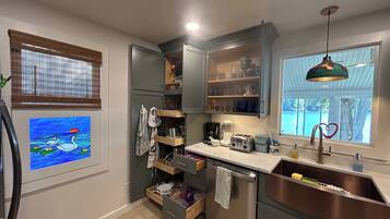 A compact kitchen with a built-in dishwasher, a stainless steel sink, and a window with a view of the outdoors.