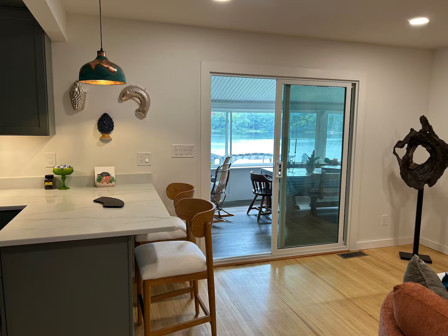 Una cocina moderna con encimera blanca, sillas de madera y vistas a un espacio exterior a través de una puerta de vidrio.