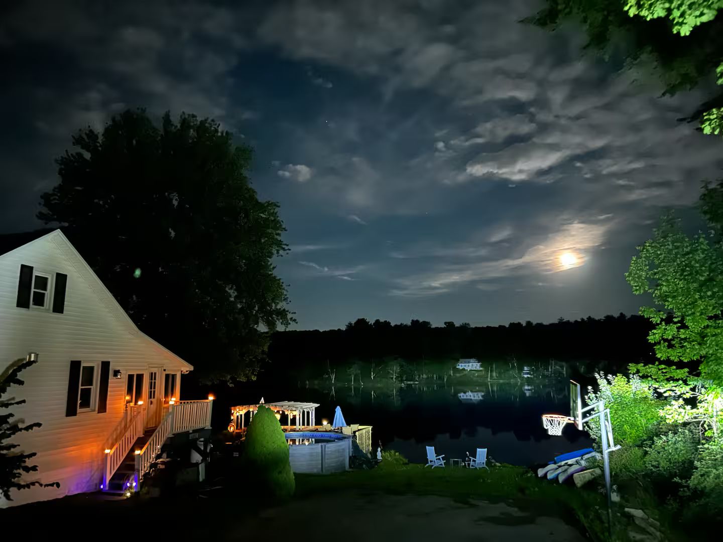 Een huis met terras en zwembad, omgeven door bomen en een meer.