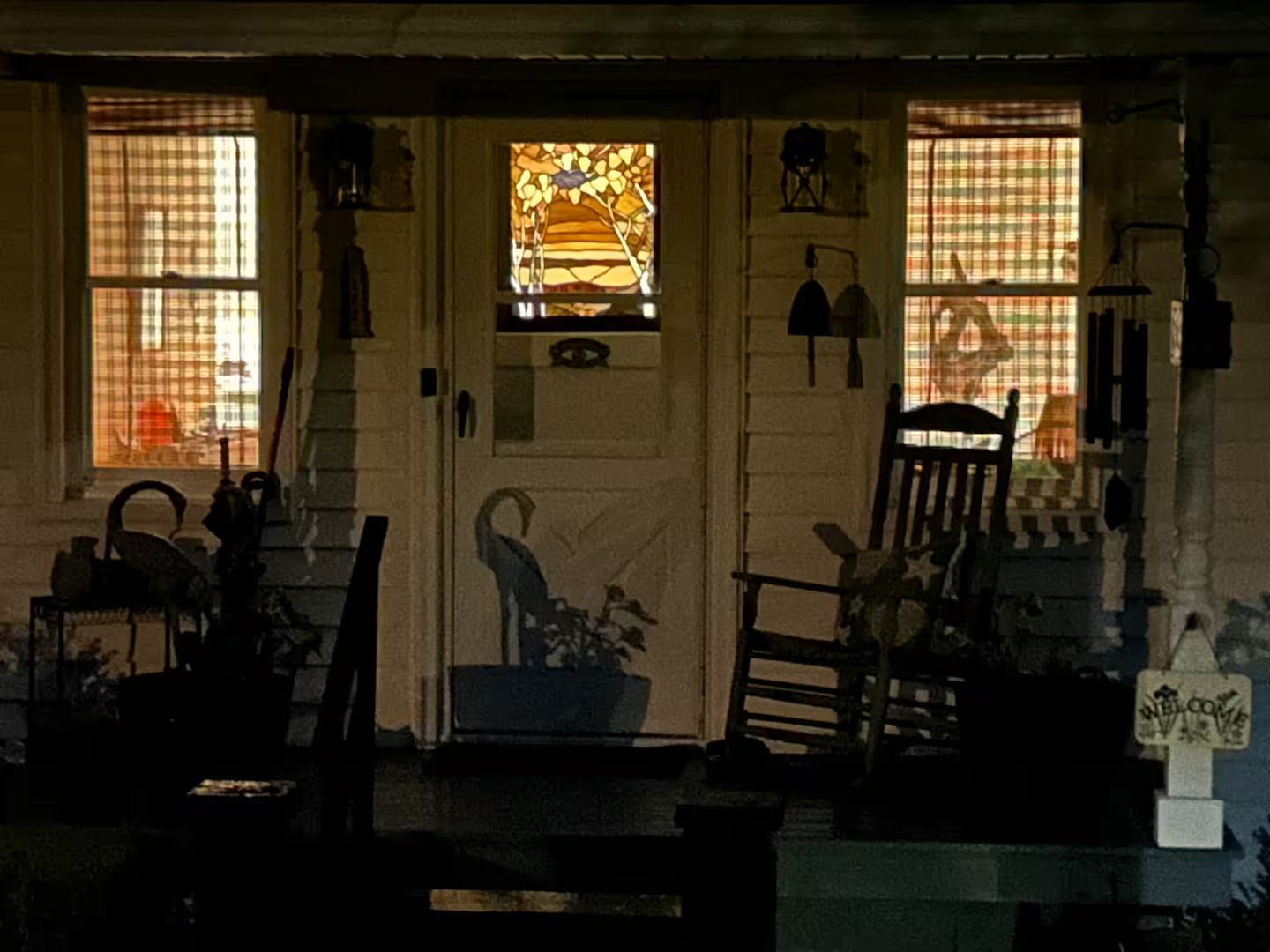 A porch with a door, two windows with curtains, a chair, and a welcome sign.