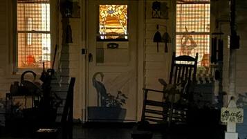 A porch with a door, two windows with curtains, a chair, and a welcome sign.
