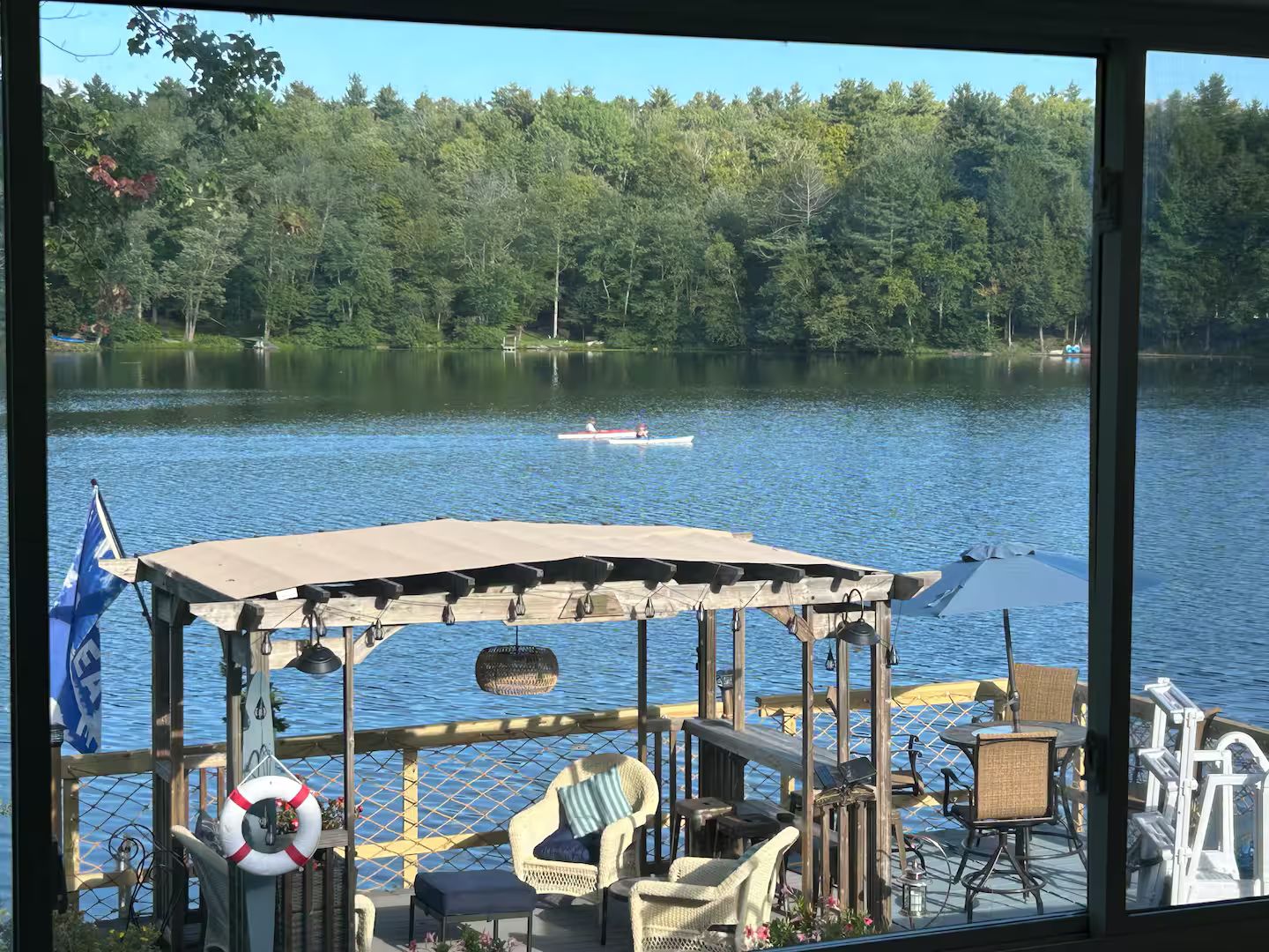 Terraza junto al lago con mobiliario exterior, una zona de estar cubierta y vistas a un lago con un bote.