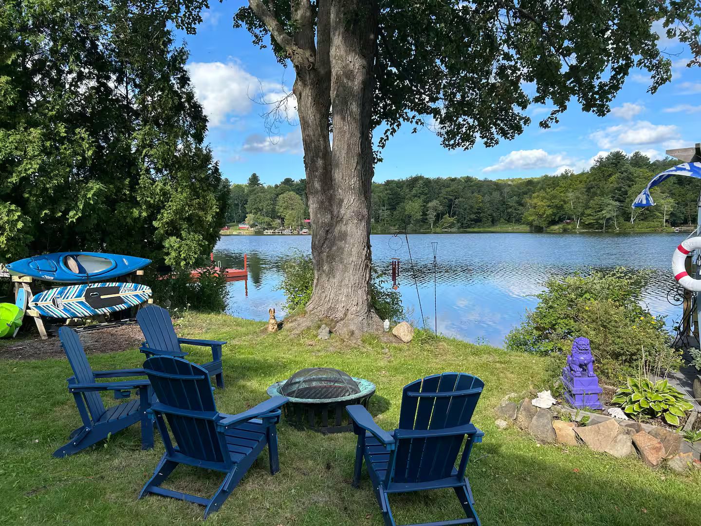Een zitgedeelte aan het meer met Adirondack-stoelen, een klein tafeltje, kajaks en hengels.