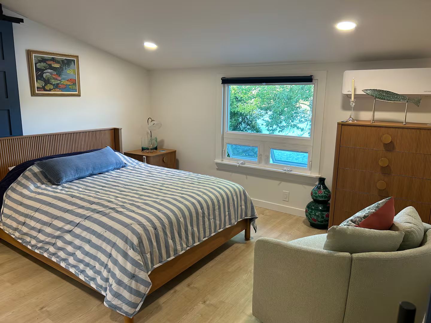 Ein Schlafzimmer mit einem Bett, einem Nachttisch, einem Fenster mit Blick, einer Kommode und einem Sessel.