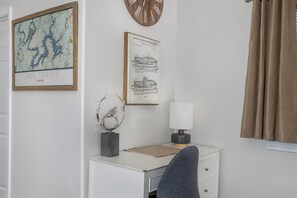 A room with a white desk, a framed map of Lake Travis, Texas, a patent office drawing, a wall clock, and a window with brown curtains. - Immaculate 3BR close to Lake with Game Room | Comfortably sleeps 8! (Lago Vista)