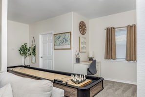 A room with a shuffleboard table, a door, a map, a clock, a window with curtains, and a small desk with a lamp. - Immaculate 3BR close to Lake with Game Room | Comfortably sleeps 8! (Lago Vista)