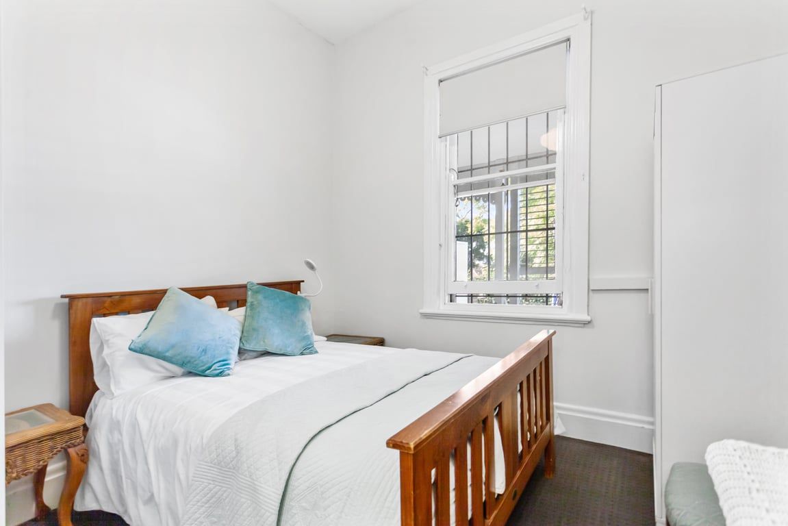 A bedroom with a wooden bed, white bedding, a window with bars, and a white door.