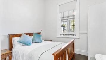 A bedroom with a wooden bed, white bedding, a window with bars, and a white door.