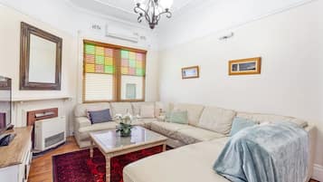 A living room with a sofa, a coffee table, and a radiator. There is a window with blinds and a chandelier.