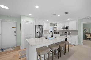 A modern kitchen with white cabinetry, stainless steel appliances, and a central island with bar stools.