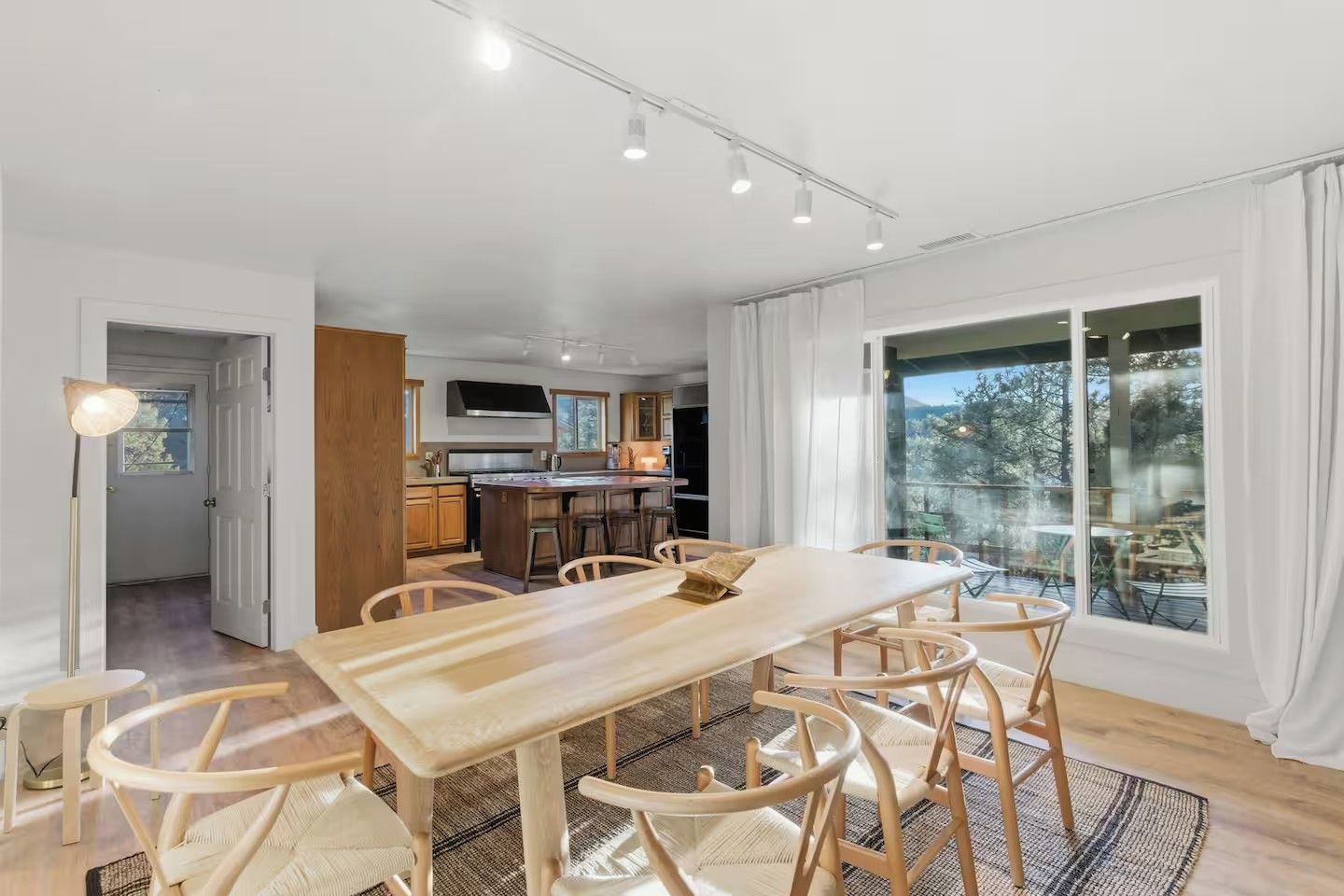 Cozinha moderna com ilha central, mesa de jantar de madeira com cadeiras e amplas janelas com vista para o exterior.