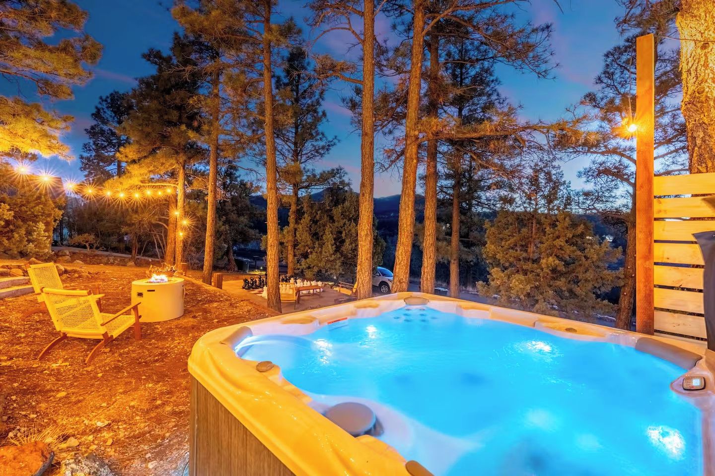 Un jacuzzi rodeado de altos árboles y una terraza de madera con sillas.