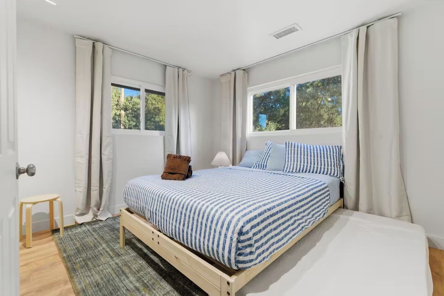 Une chambre à coucher avec un lit, une fenêtre, une porte et un petit tabouret.