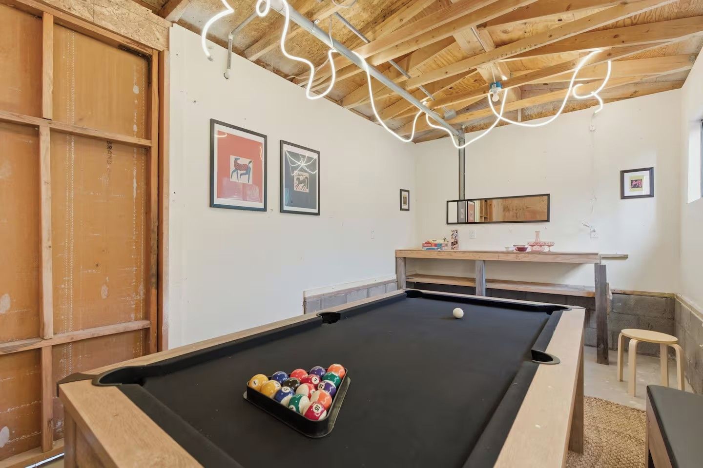 A pool table with a set of balls, wooden walls, and framed artwork.