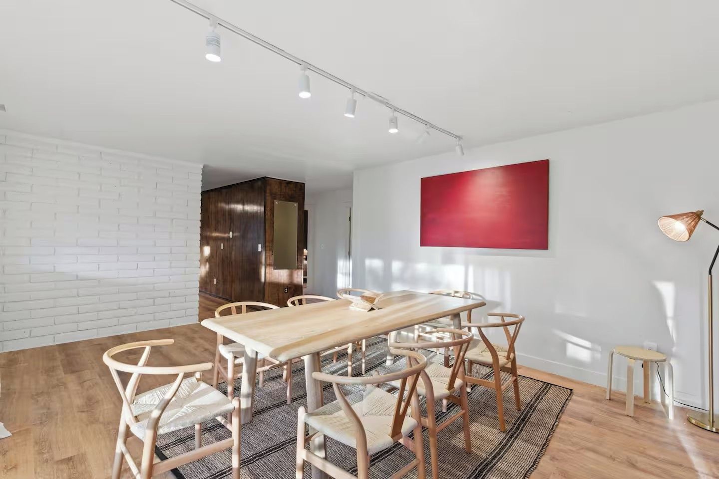 A modern dining area with a wooden table and chairs, a red accent wall, and a floor lamp.