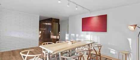 A modern dining area with a wooden table and chairs, a red accent wall, and a floor lamp.