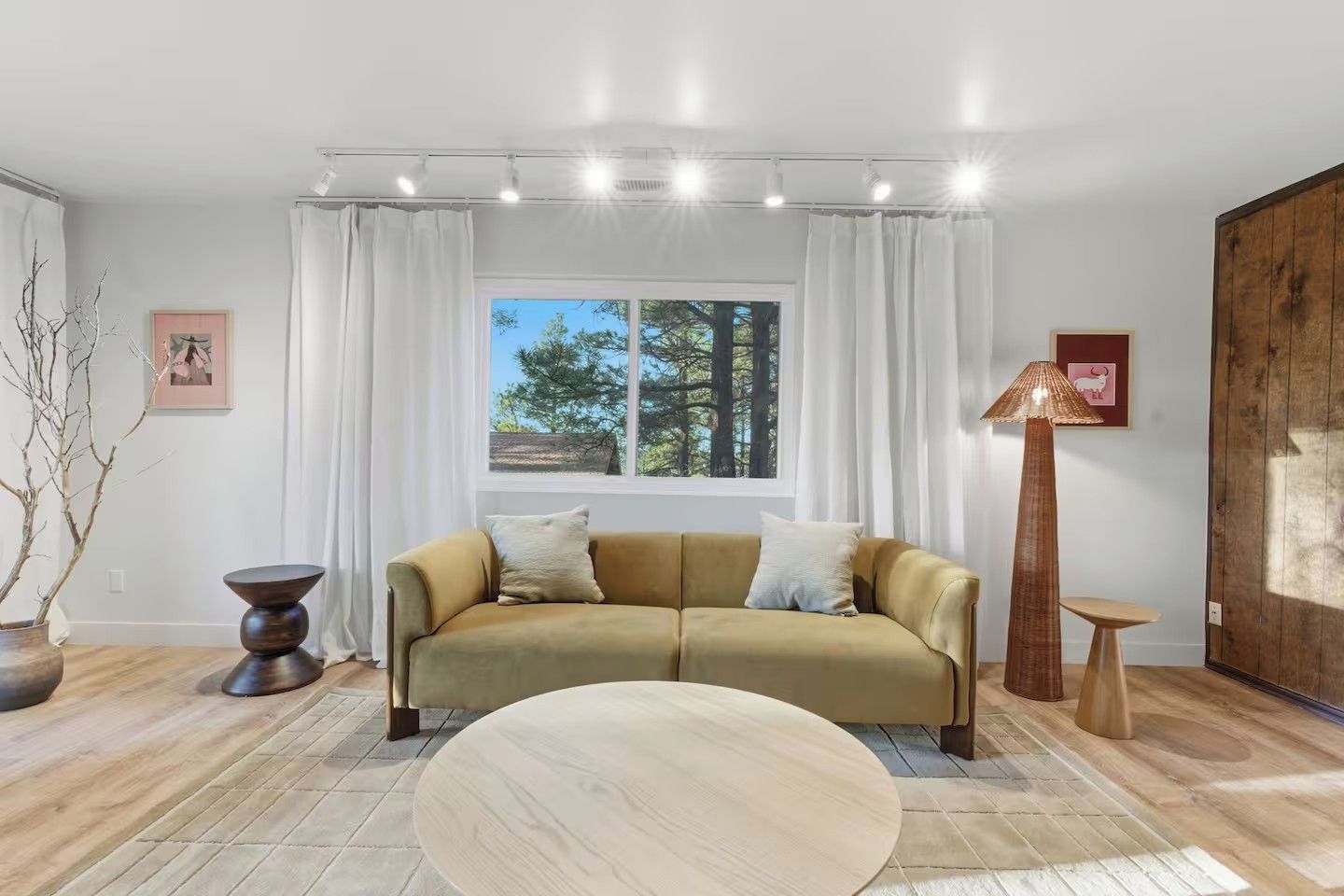 A modern living room with a sofa, a round coffee table, a tall floor lamp, and a window with curtains.