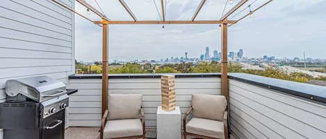 Terraço no telhado com churrasqueira, duas cadeiras, lareira e vista para o horizonte da cidade.