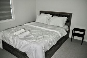 A bed with a wooden frame, white bedding, and a rolled towel. - Luxury 4BR Detached Home 4 Beds plus 2 Sofa Bed Sleeps 10 Close to Niagara Falls (Thorold)