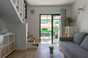 Ein modernes Wohnzimmer mit einem grauen Sofa, einer Treppe und Blick ins Freie.