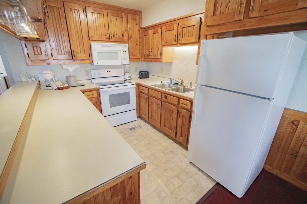 A kitchen with wooden cabinets, a white refrigerator, a microwave, an oven, and a sink.