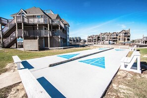Ein Hotel direkt am Strand mit einer Holzterrasse, einem Rettungsturm und einer Promenade mit blauen Hinweisschildern.