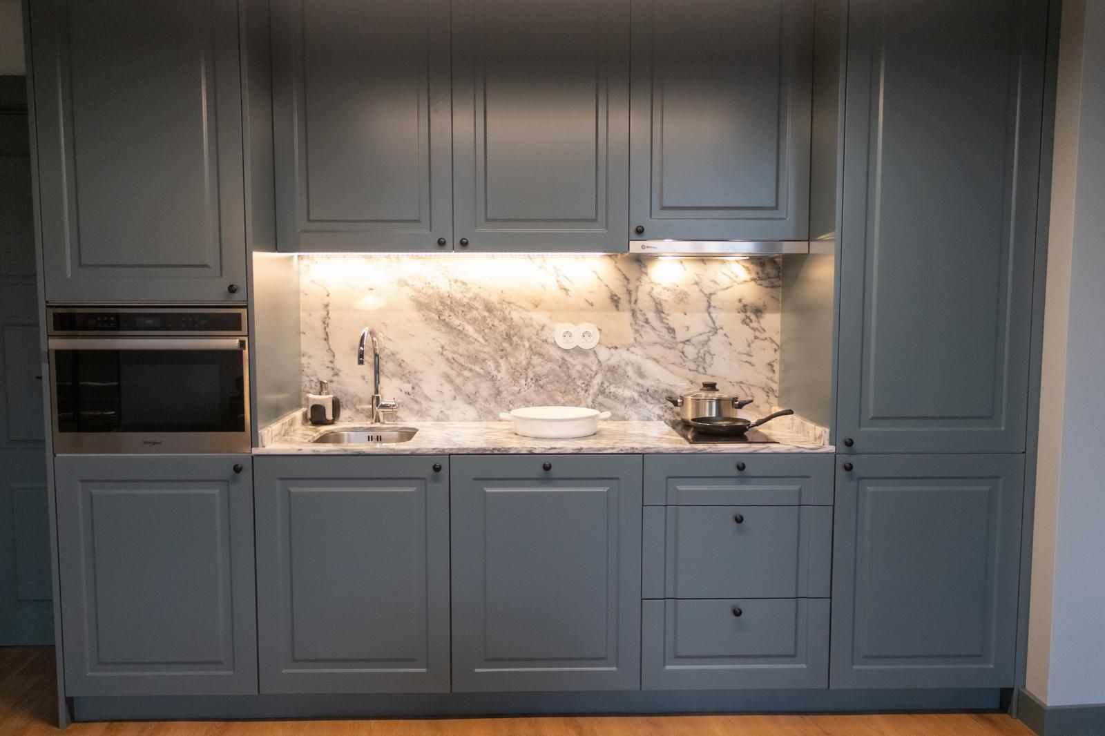 Een keuken met grijze kastjes, een marmeren spatwand en roestvrijstalen apparatuur.