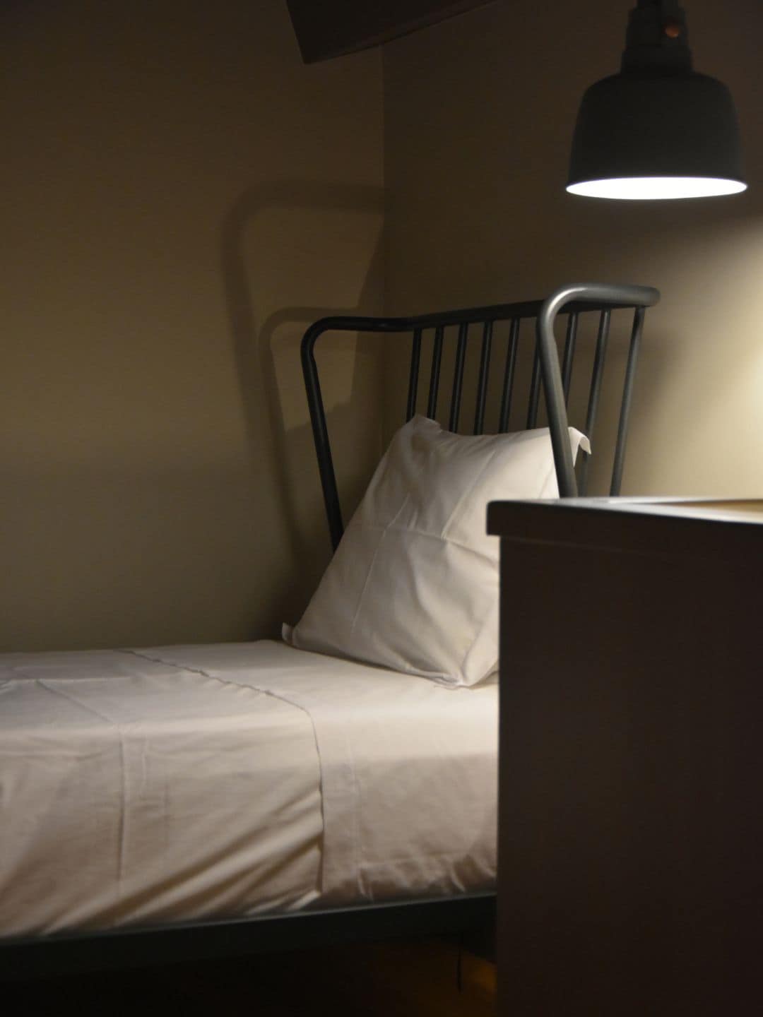 A single bed with a metal frame and white bedding, under a hanging lamp.