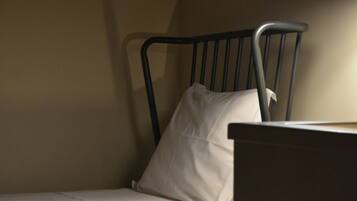 A single bed with a metal frame and white bedding, under a hanging lamp.