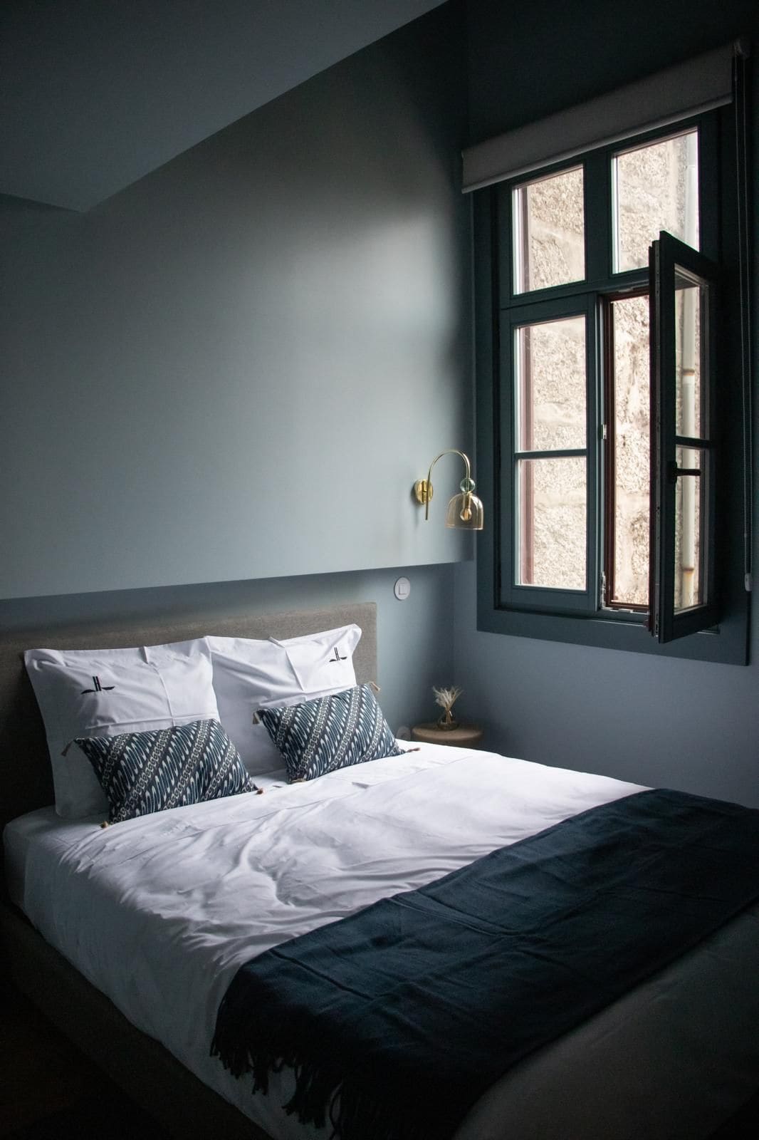 Quarto com cama, mesa de cabeceira, abajur e janela.