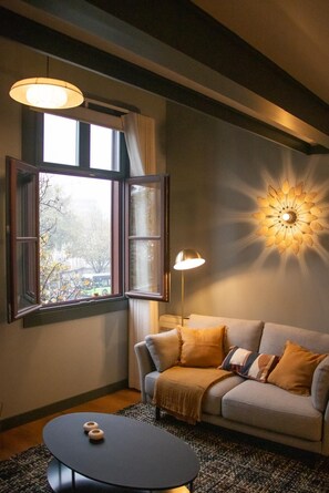 A living room with a sofa, a round coffee table, a floor lamp, and a wall-mounted light fixture.
