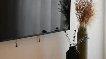 A flat-screen TV mounted on a wall above a wooden console with a cactus and a vase with dried plants.