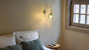 Un dormitorio con cama, almohadas, una mesita de noche con control remoto y una ventana con persianas.