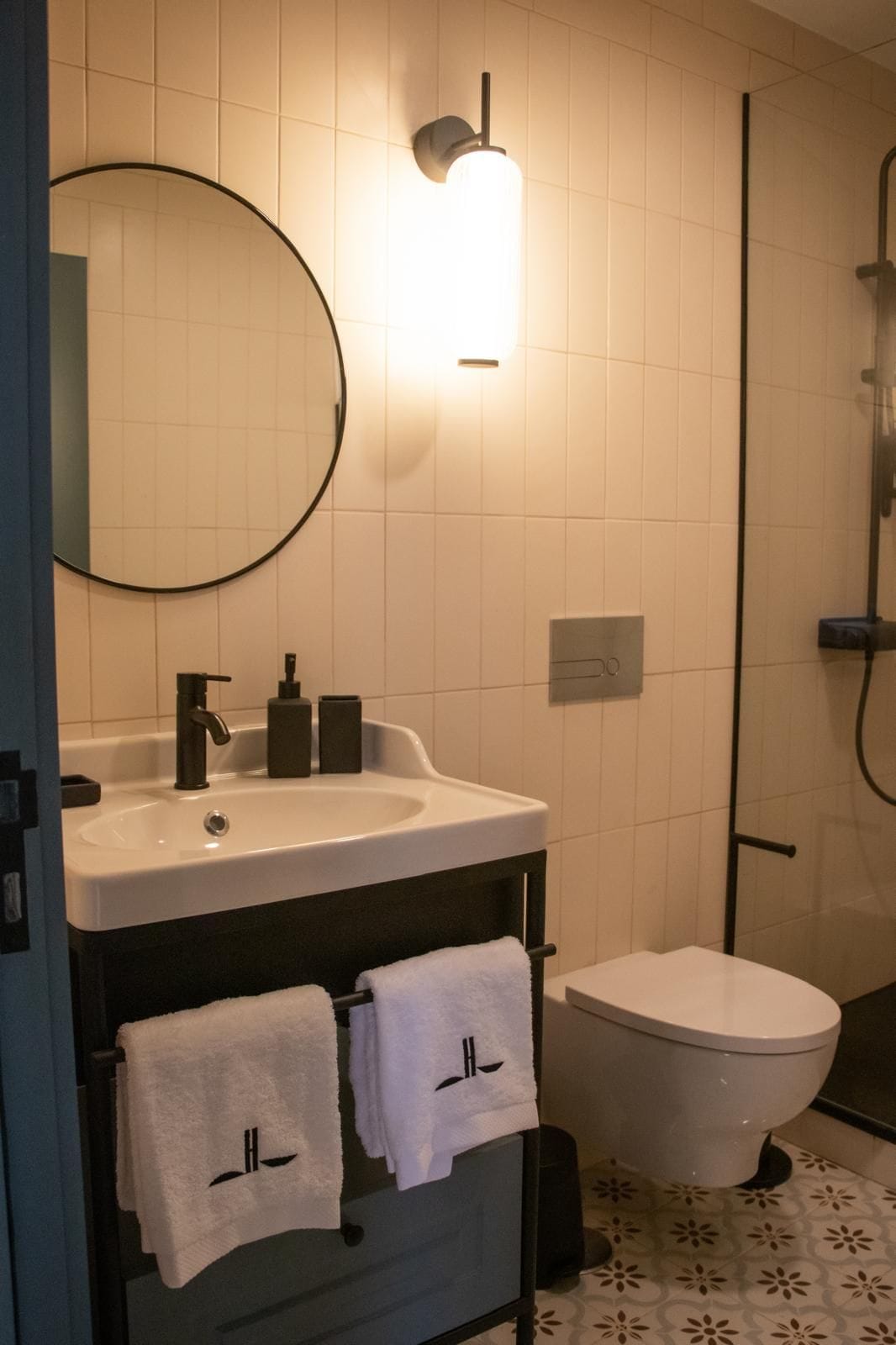 A modern bathroom with a round mirror, a white sink, a toilet, and a shower area.