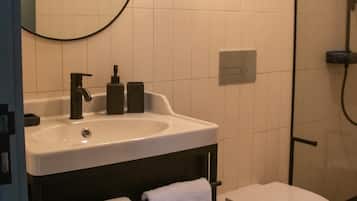 A modern bathroom with a round mirror, a white sink, a toilet, and a shower area.