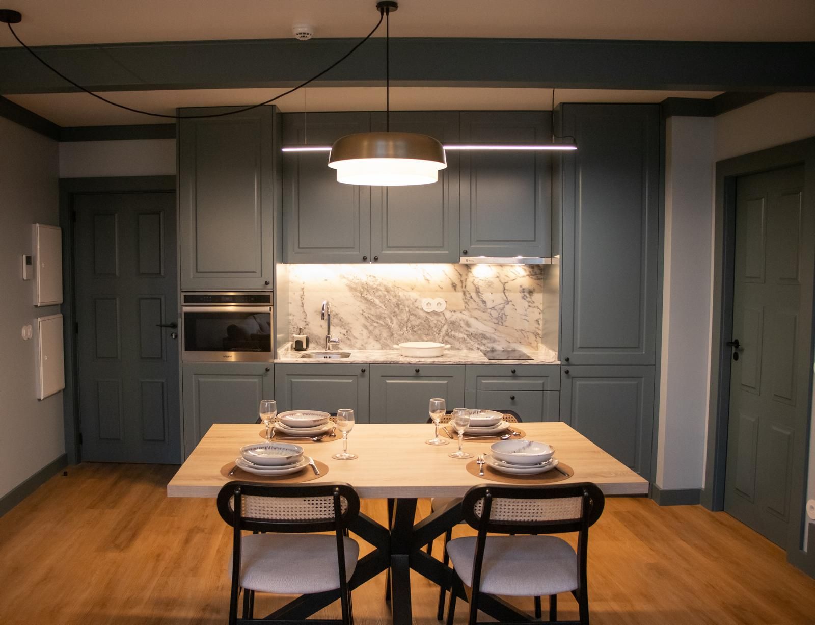 A modern kitchen with grey cabinets, a marble countertop, and a dining table set for four.