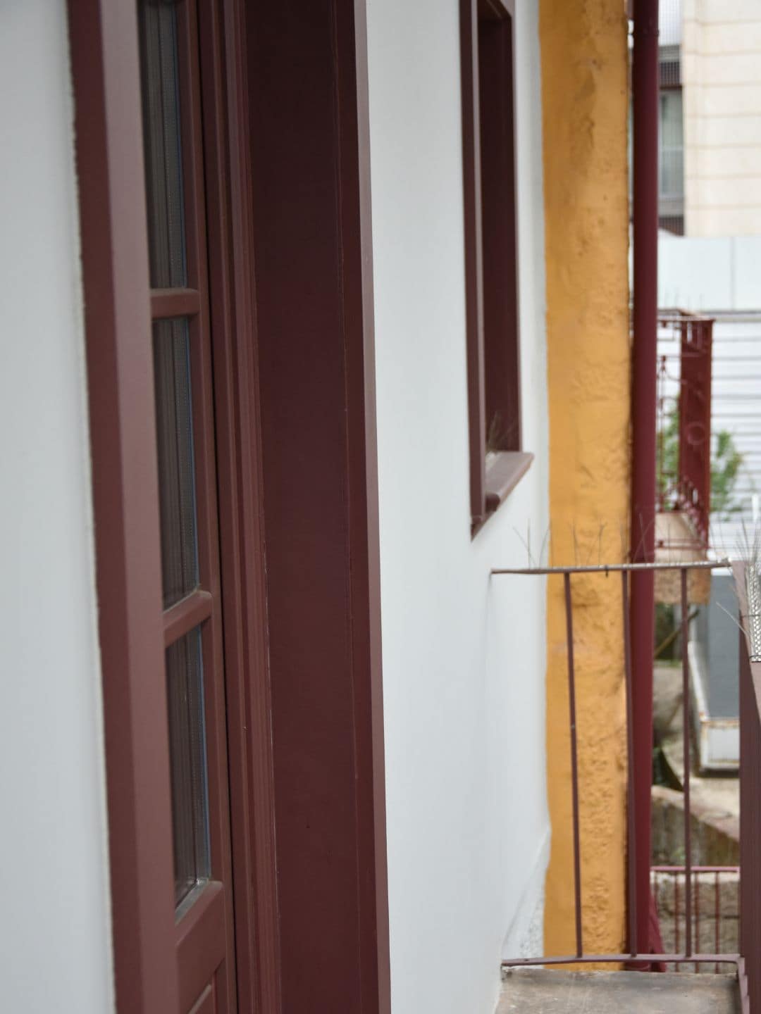 A narrow corridor with a window on the left and a balcony with a railing on the right.
