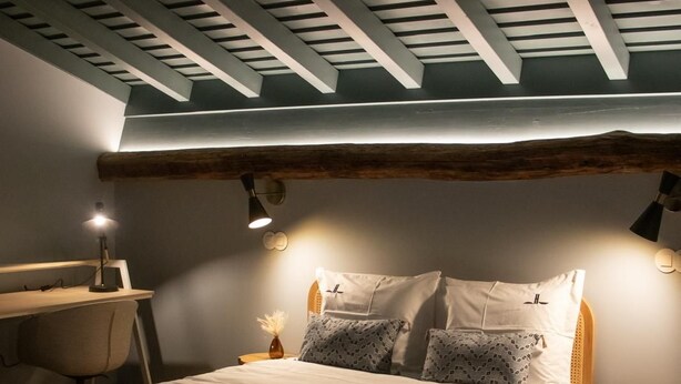 Un dormitorio con techo inclinado, una cama con muchas almohadas, un escritorio y una silla.